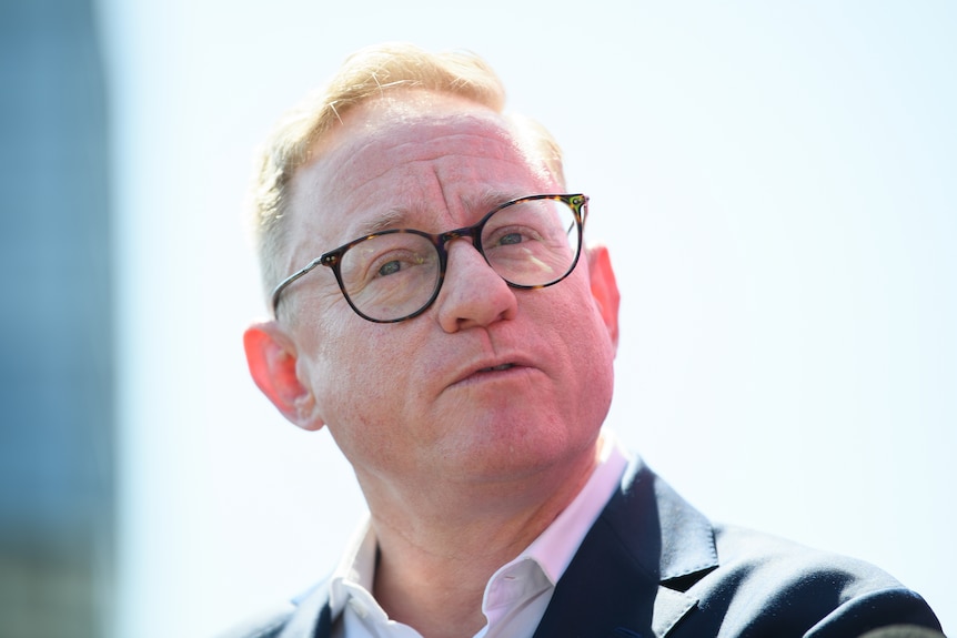 a man wearing glasses talking to the press outdoors