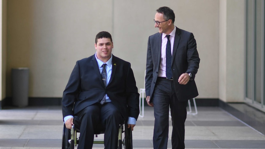 Jordon Steele-John, in his wheelchair, outside Parliament House with Richard di Natale. They are both wearing suits.