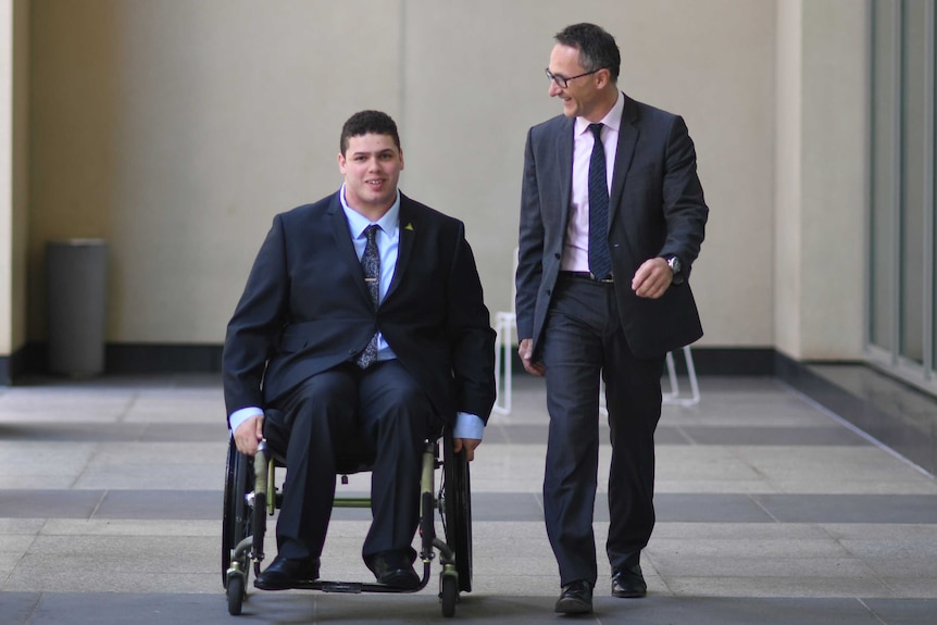 Jordon Steele-John, in his wheelchair, outside Parliament House with Richard di Natale. They are both wearing suits.