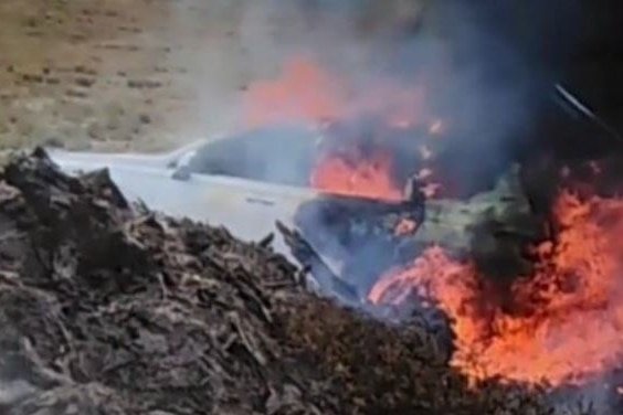 the burnt shell of a car, with flames and smoke.