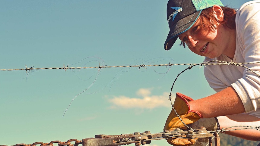 Teen fixing a barbed wire fence on a farm to depict why we need to understand Australians' experiences outside the city bubble