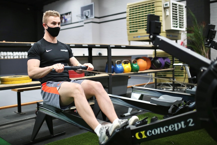 A man wears a black COVID mask while working out on gym equipment.