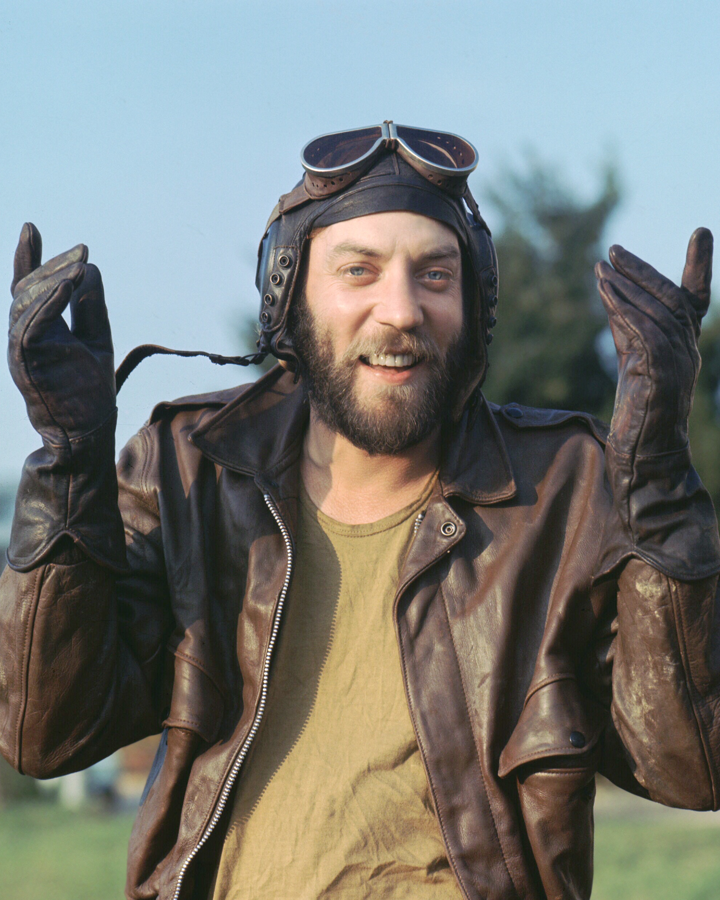 Donald Sutherland with his hands in the air, wearing a helmet and googles 
