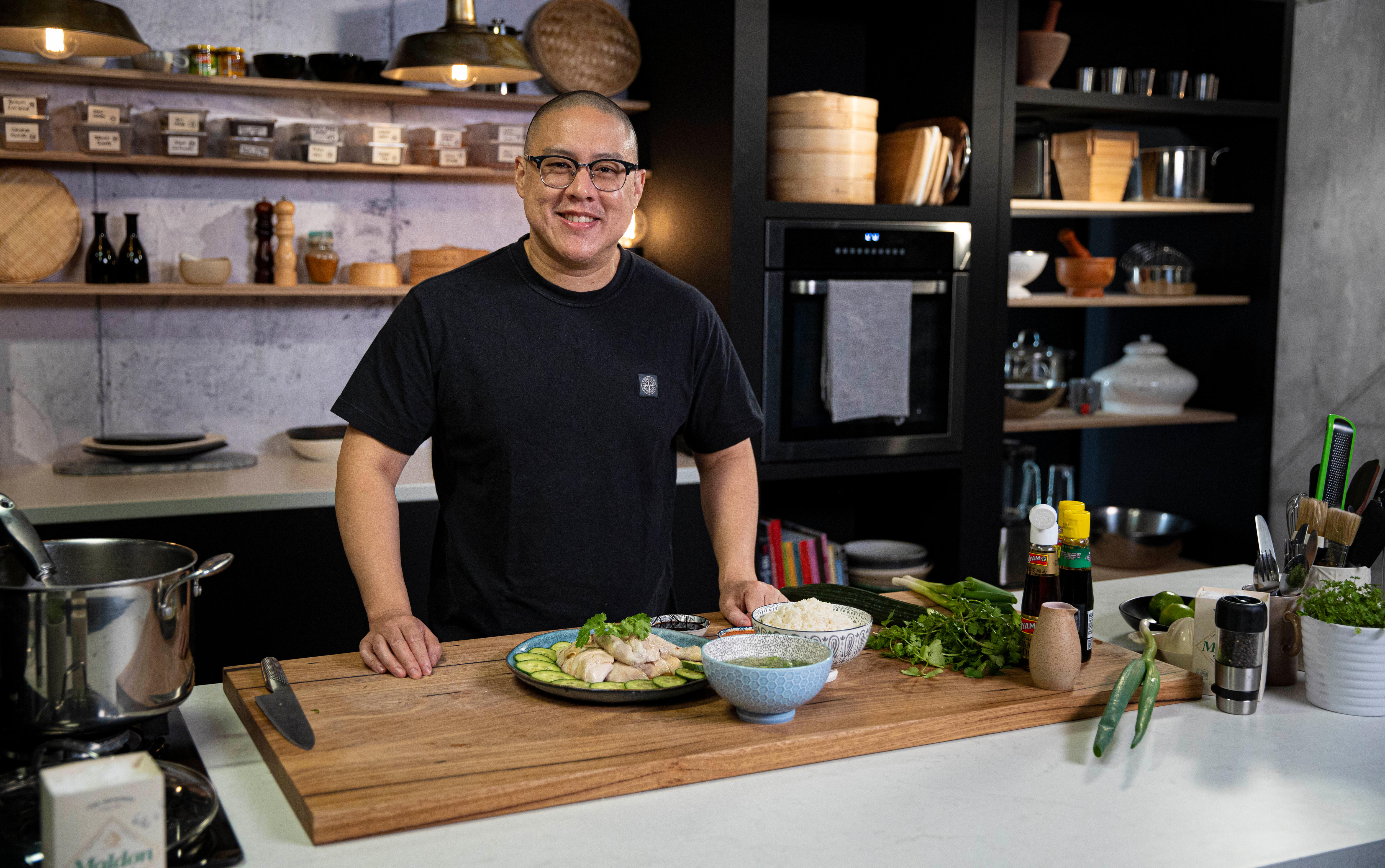 Man stands in kitchen wears black tee. 