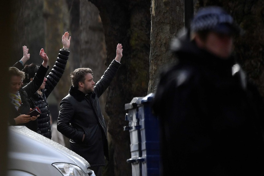 People standing on a street in coats wave.