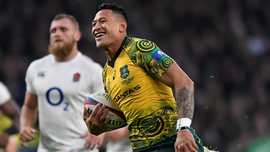 Israel Folau, wearing a gold jersey, smiles as he runs with a rugby ball under his arm