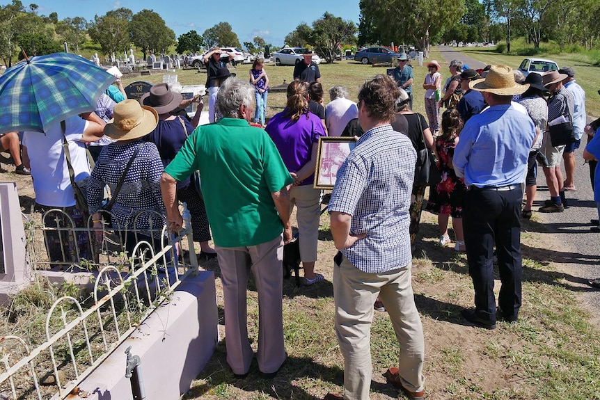 A group of people gather around a grave at Belgian Gardens Cemetery for a memorial service for Annie Ferdinand.