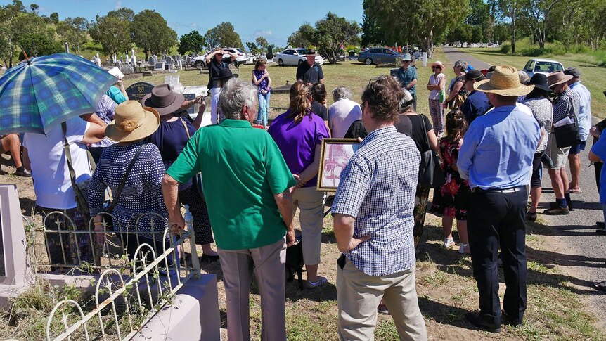 A group of people gather around a grave at Belgian Gardens Cemetery for a memorial service for Annie Ferdinand.