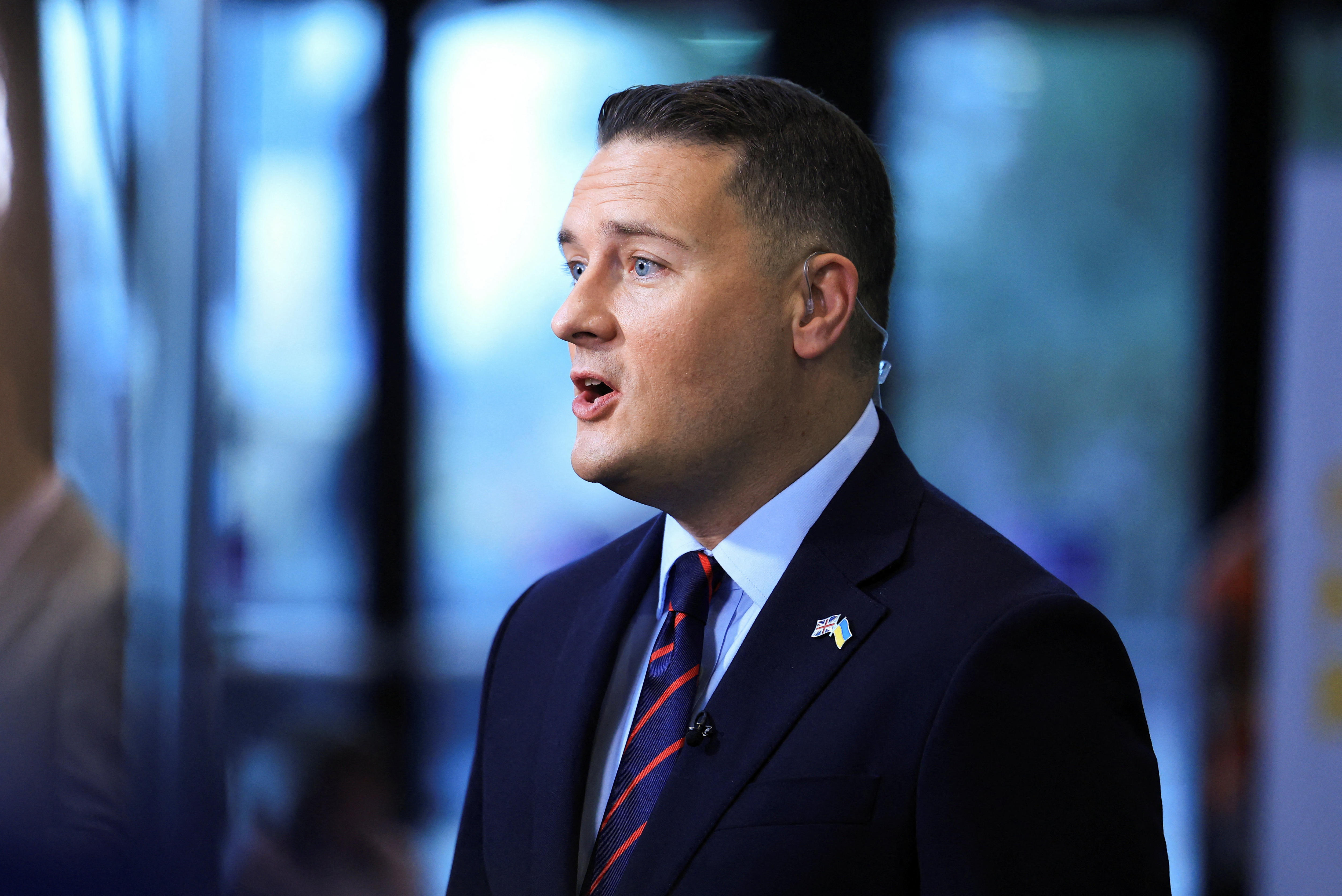 A man in a suit speaking to journalists.