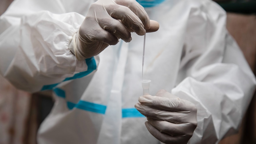 A person wearing a white protective suit holds a sample above a tube.