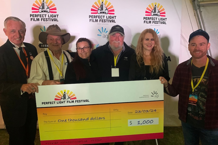 A line of men and women holding a big cheque