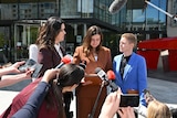 Journalists gather around a woman giving a press conference. 