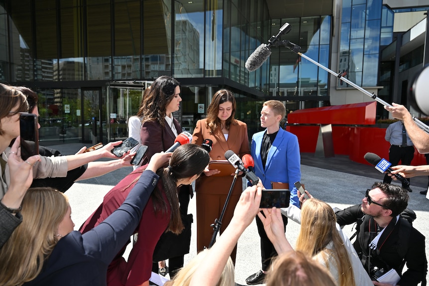 Journalists gather around a woman giving a press conference. 