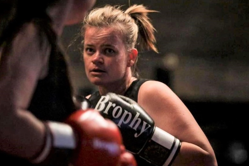 A woman wearing boxing gloves stands in a fighting position.