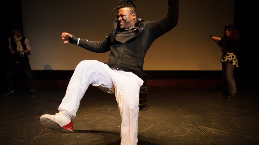 A young black man falls back wards onto a dark stage.