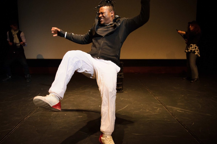 A young black man falls back wards onto a dark stage.