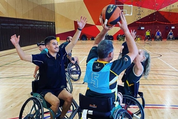 Three people reaching to grab a volleyball. They are using wheelchairs.