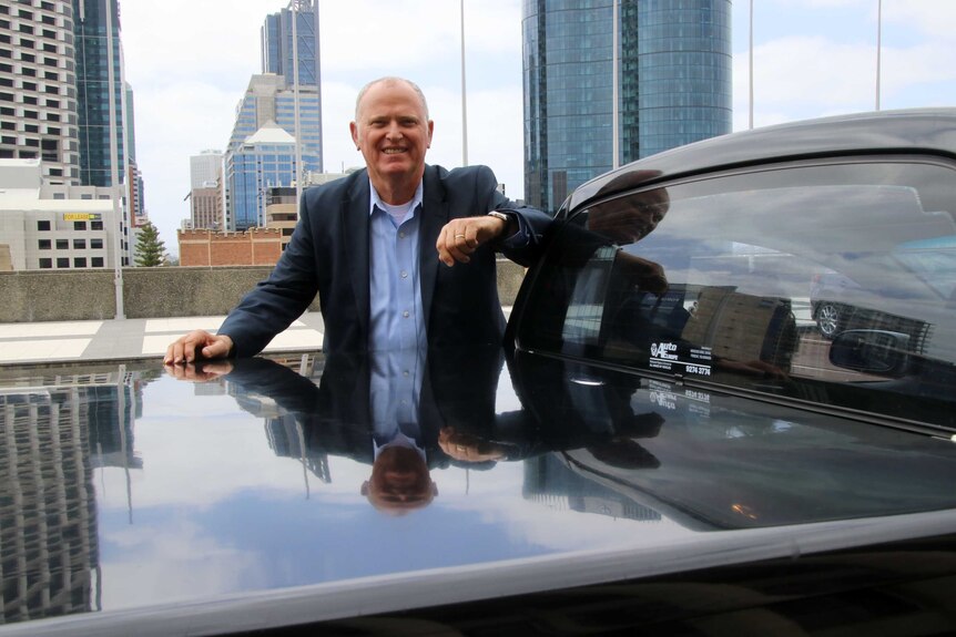 Ian Britza next to his car with Perth city buildings in the background.
