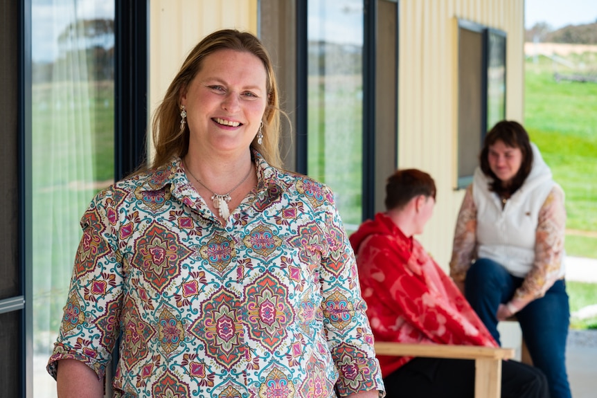 A woman smiles at the camera with her two daughters in the background