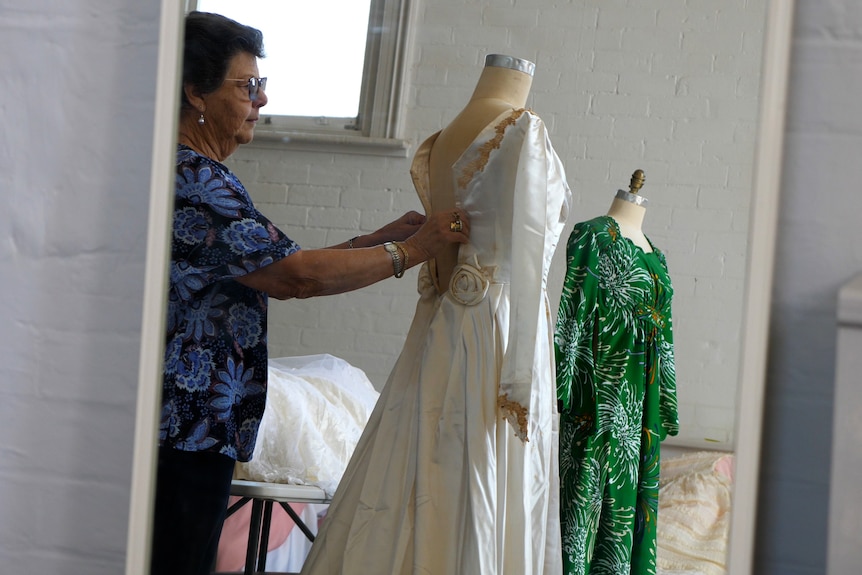 a woman zipping up the back of a white wedding dress on a mannequin