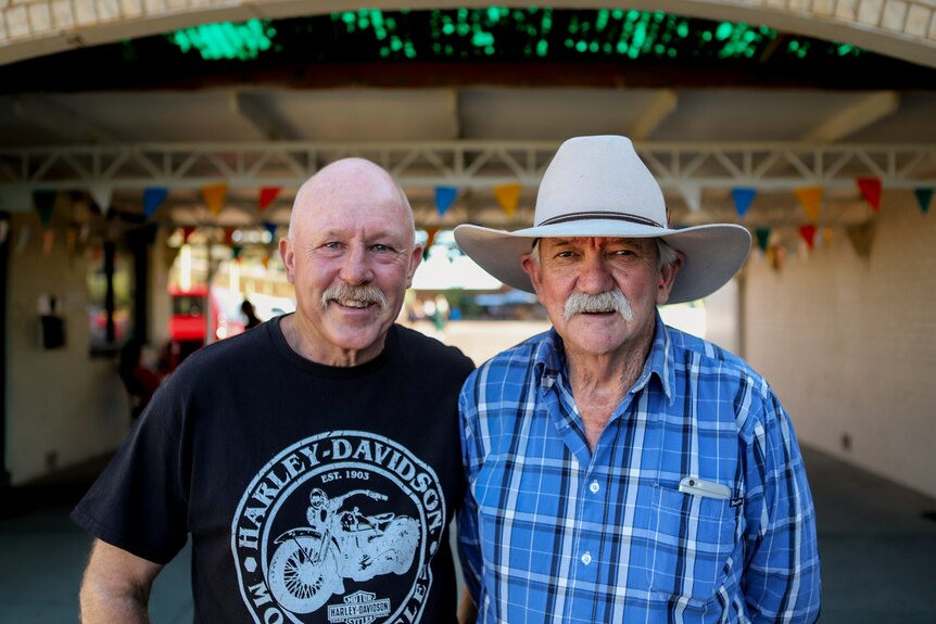 Two older men standing outside a motel, one wearing a cowboy hat
