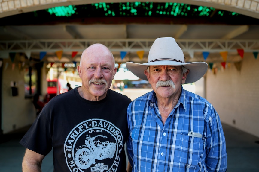 Two older men standing outside a motel, one wearing a cowboy hat