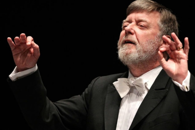 Sir Andrew Davis conducts in white tie with his eyes closed and rapt expression.