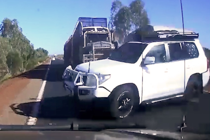 An image from dashcam footage showing a white four-wheel drive sideways on a country highway with a cattle truck behind it.
