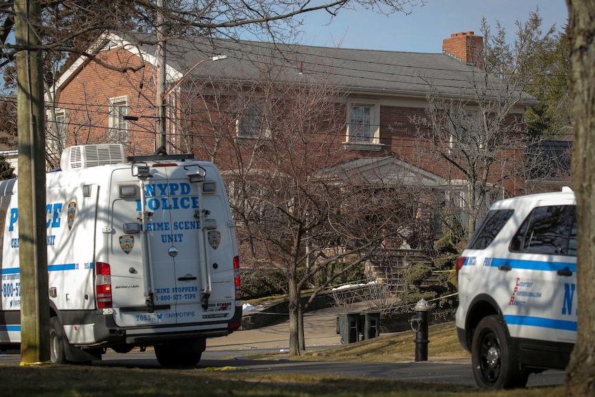 A pair of police vehicles parked outside a large double-story home with police tape blocking off the driveway.