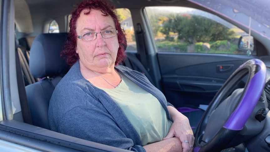 A middle-aged woman with red hair sits behind the wheel of a car