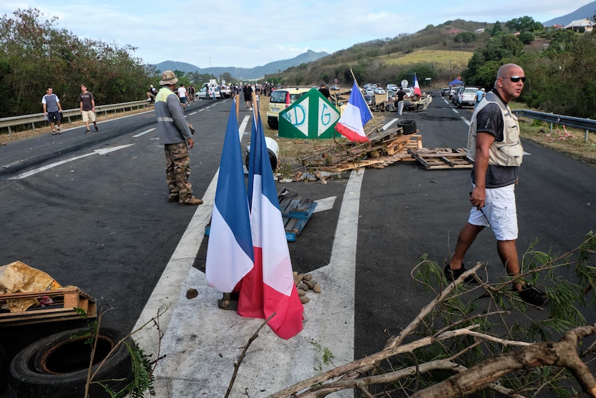 Men stand beside debris piled on the road, with French flags waving.