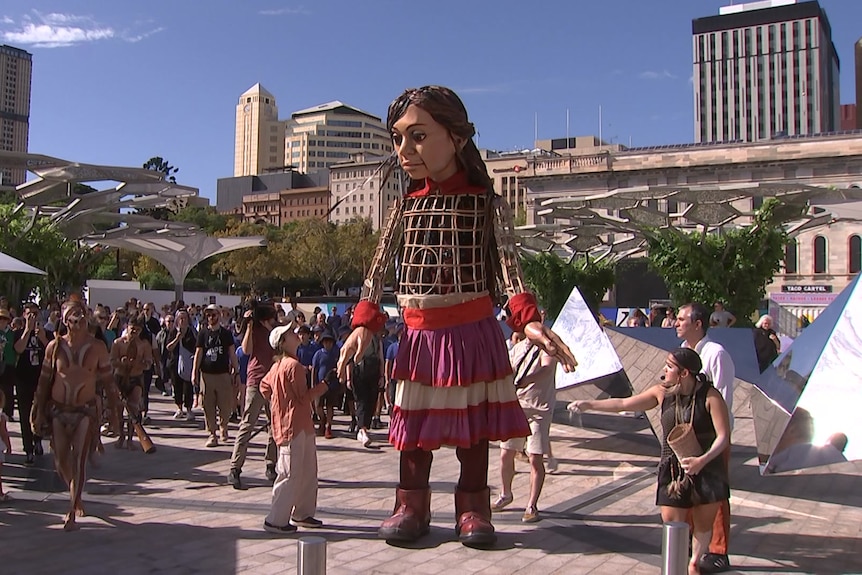 Puppet Little Amal walks among crowd of people