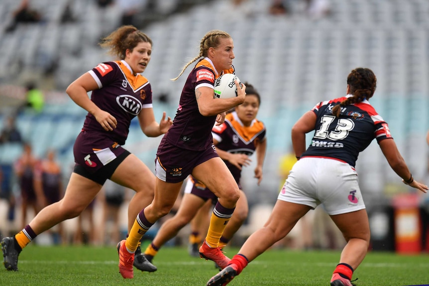 A player tucks the ball under her arm as she runs toward the tryline in an NRLW game.