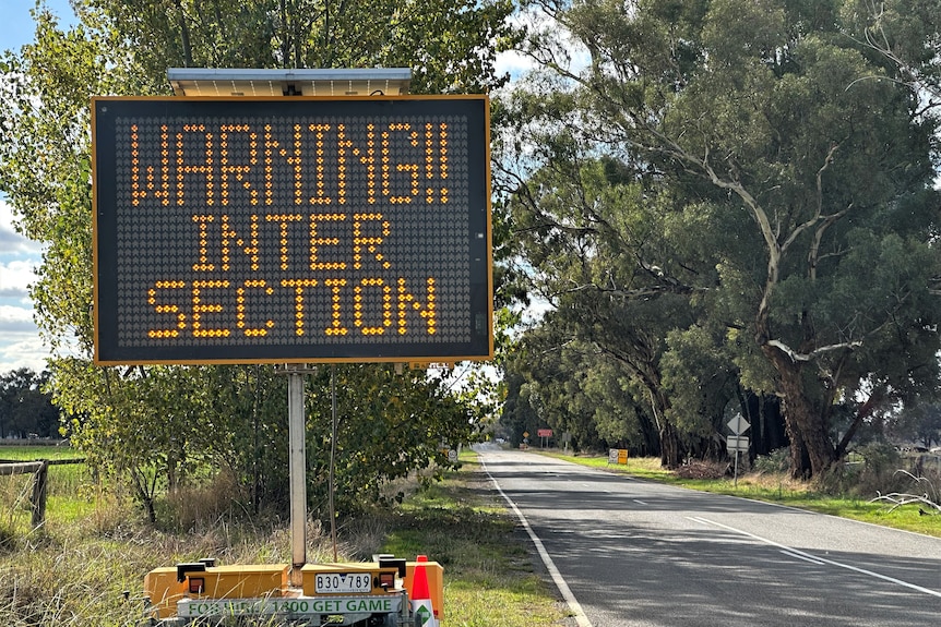 A flashing sign which says "warning, intersection" is erected next to a country road. 