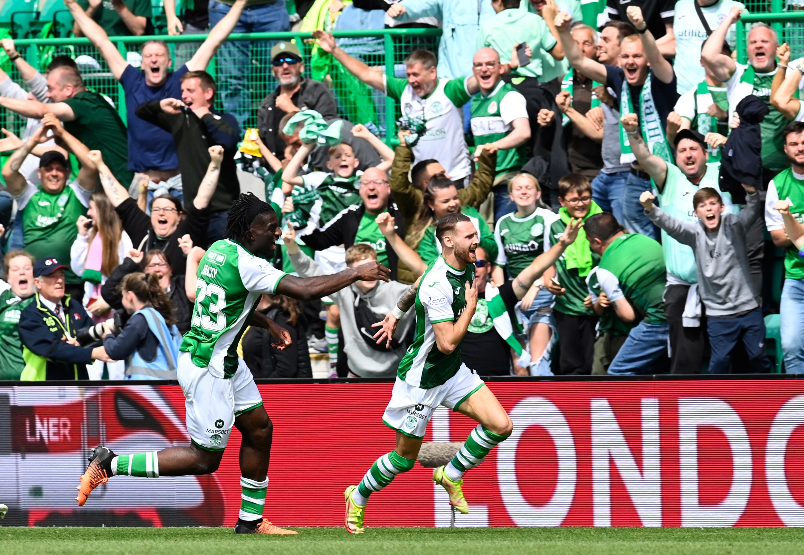 An Australian striker playing for Scottish side Hibernian runs down the touchline as ecstatic fans roar and punch the air..
