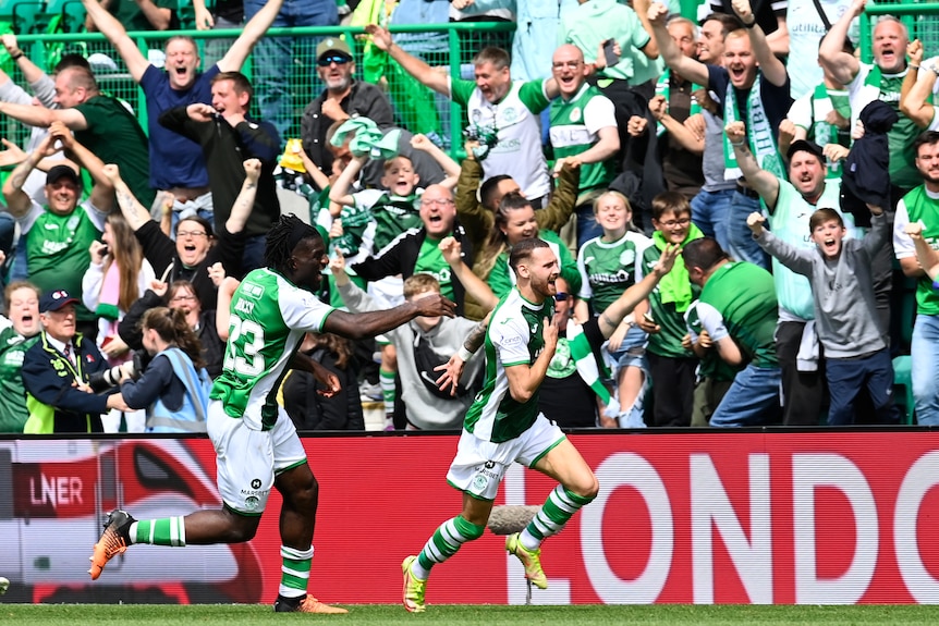 An Australian striker playing for Scottish side Hibernian runs down the touchline as ecstatic fans roar and punch the air..