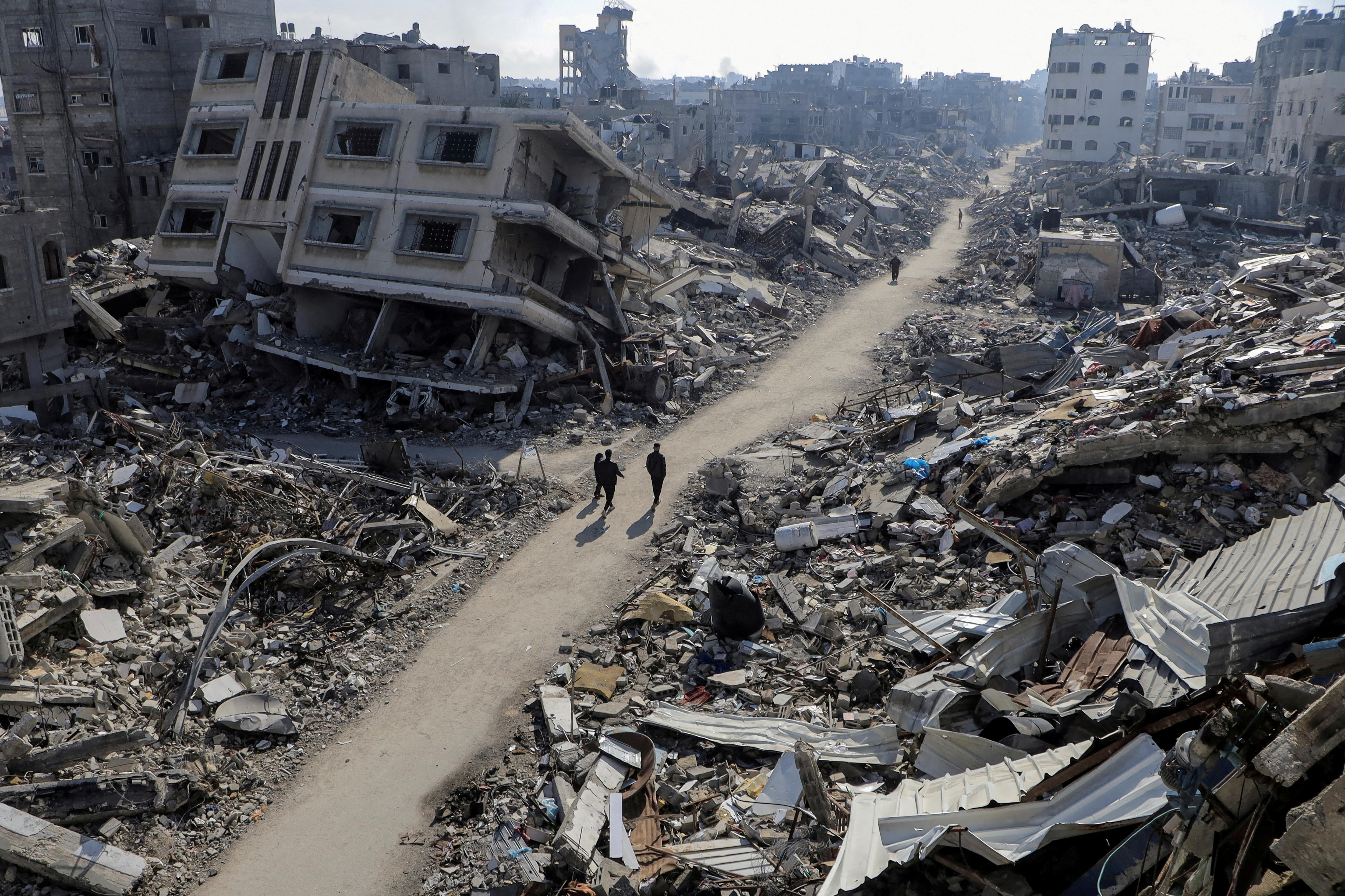 Three people walking through an area with damaged buildings