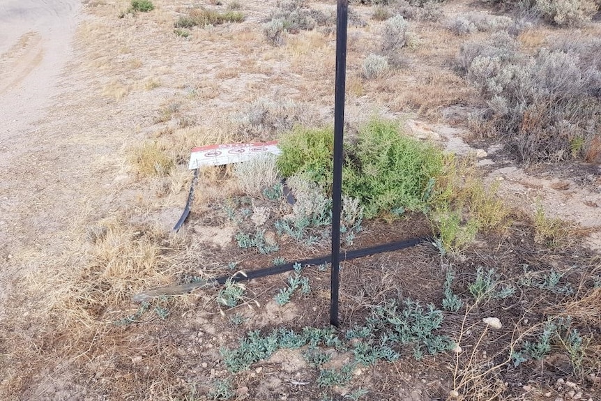 A metal pole and sign is lying on the scrub after being pulled out.