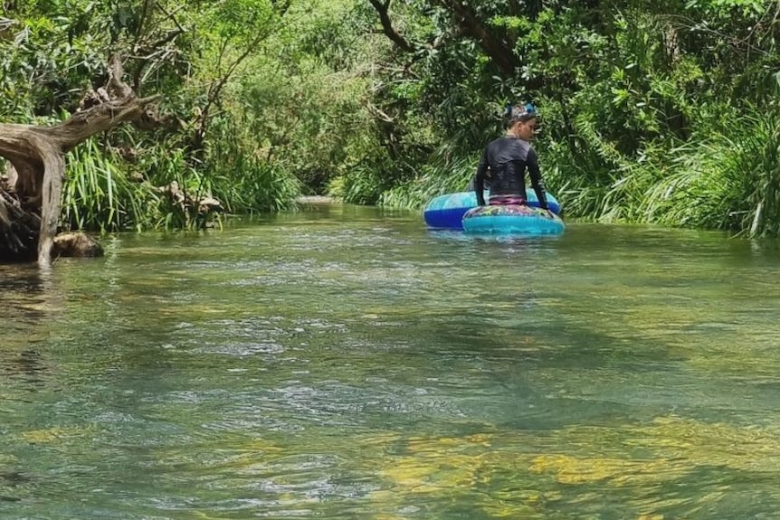 Child on inflatable raft in river with lush green banks