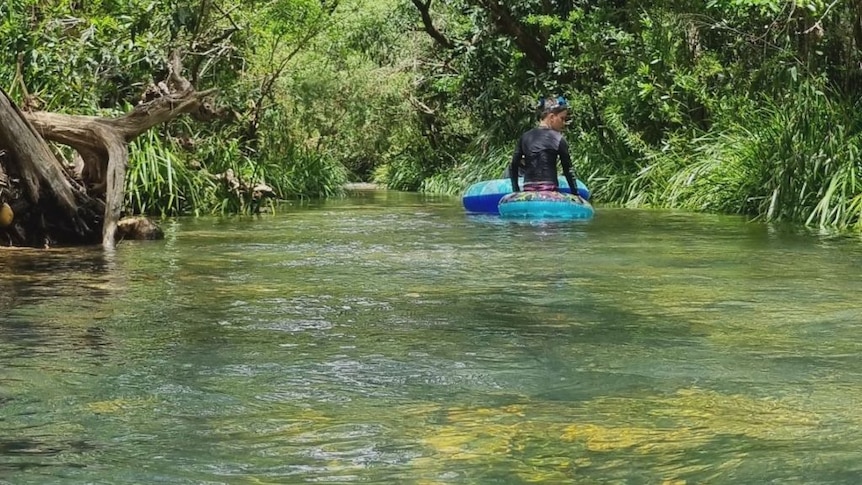 Child on inflatable raft in river with lush green banks