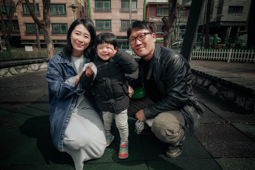 A Korean couple crouching next to a small boy giving a peace sign