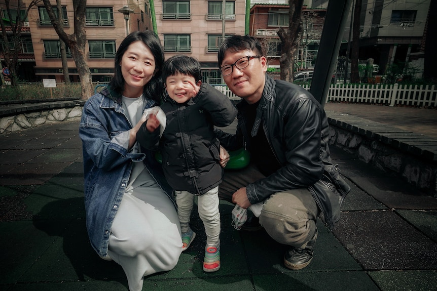 A Korean couple crouching next to a small boy giving a peace sign