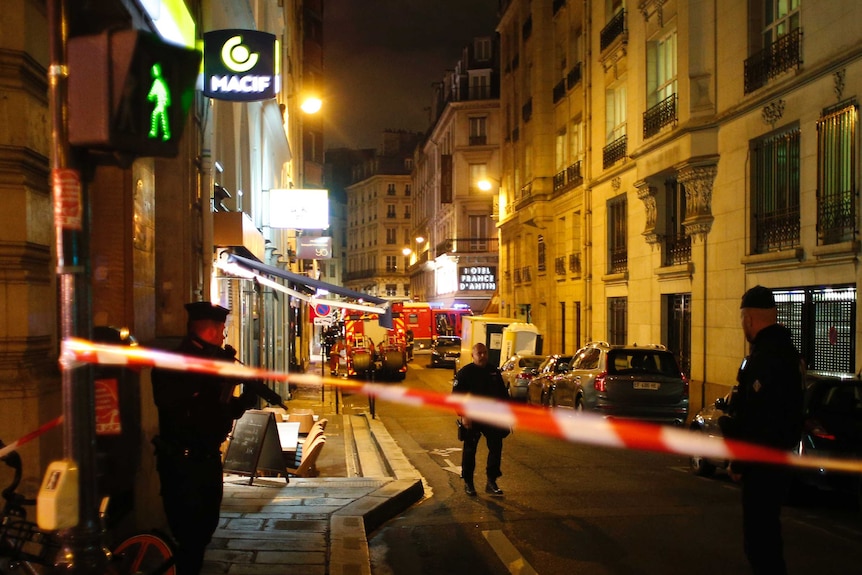 Police tape streches across a street in France where police officers with guns stand.