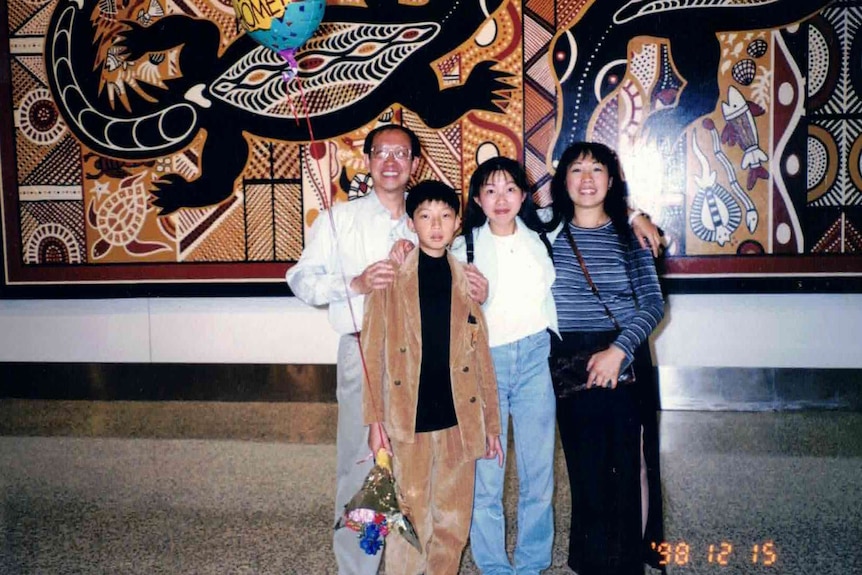 A family of four, including the father, mother, sister and younger brother standing in front of a piece of aboriginal art in NSW