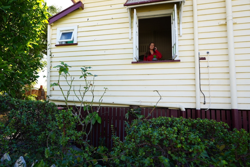 A woman is seen through the window of a home, on the phone.