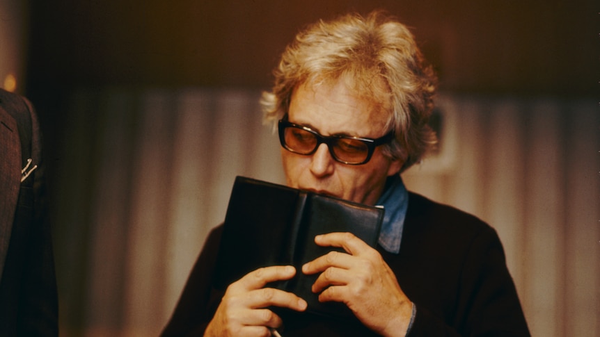 Ligeti kissing a book, wearing sunglasses inside. strong vibes.