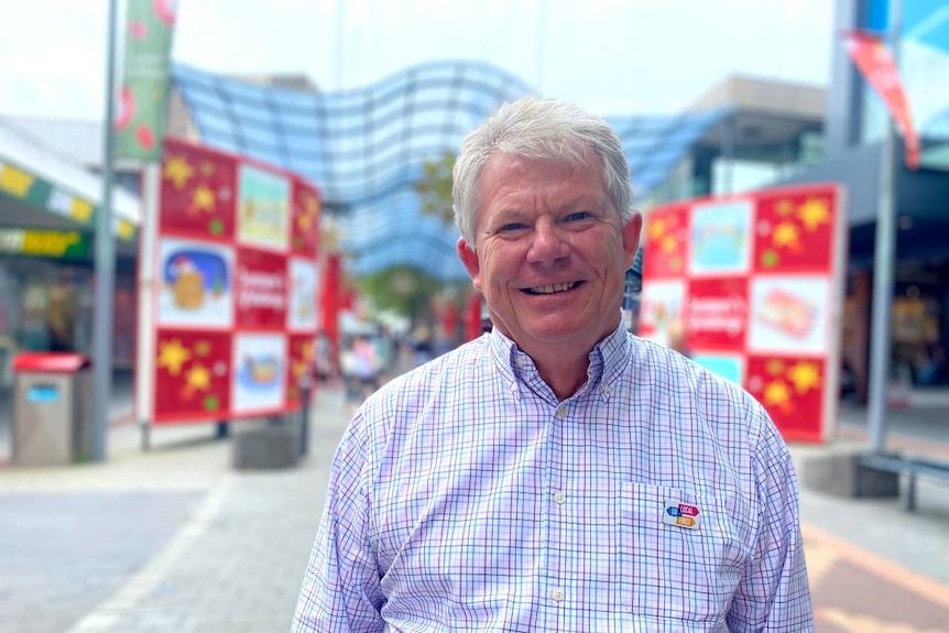 A man with silver hair wearing a check shirt stands in a shopping mall