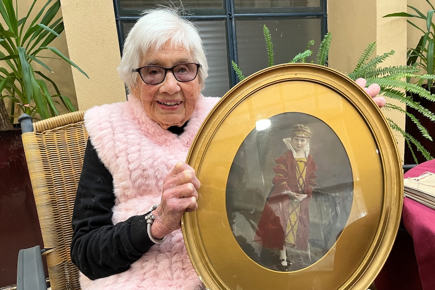An elderly woman holding an oval framed photo of a young child wearing Elizabethan costume