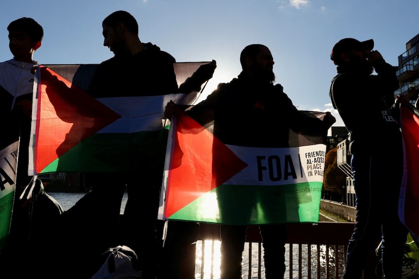 The silhouette of several people, some holidng Palestinian flags