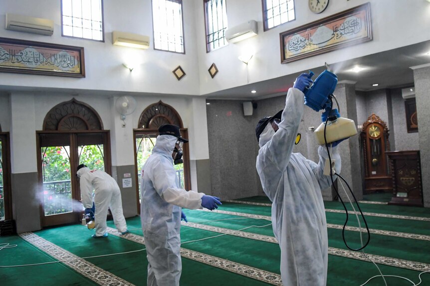People in white biohazard suits spray disinfectant inside a mosque.